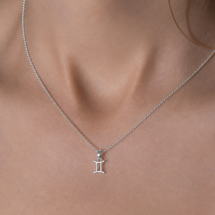 Silver necklace with a Gemini pendant on a person's neck