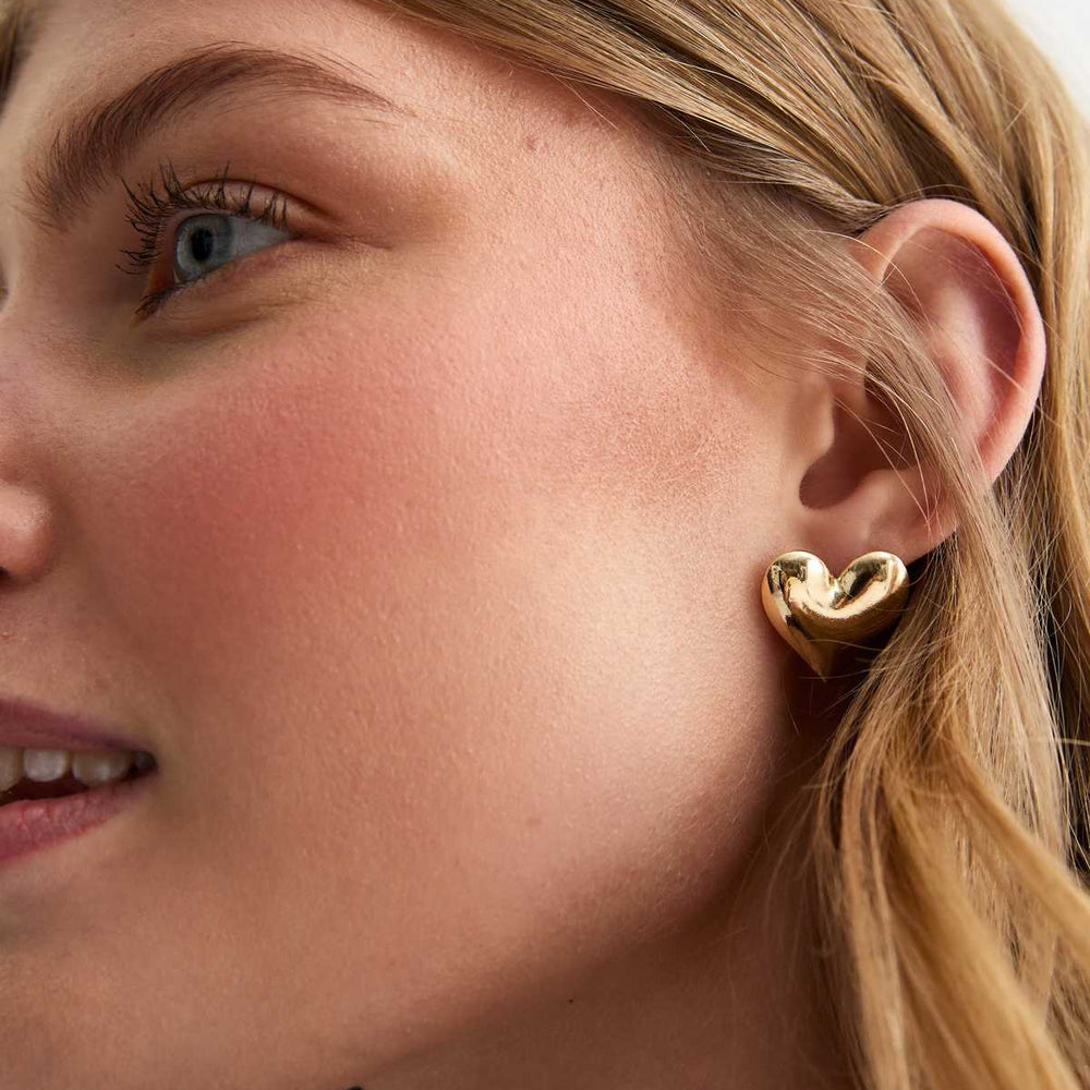 Close-up of a woman wearing a gold heart-shaped earring.