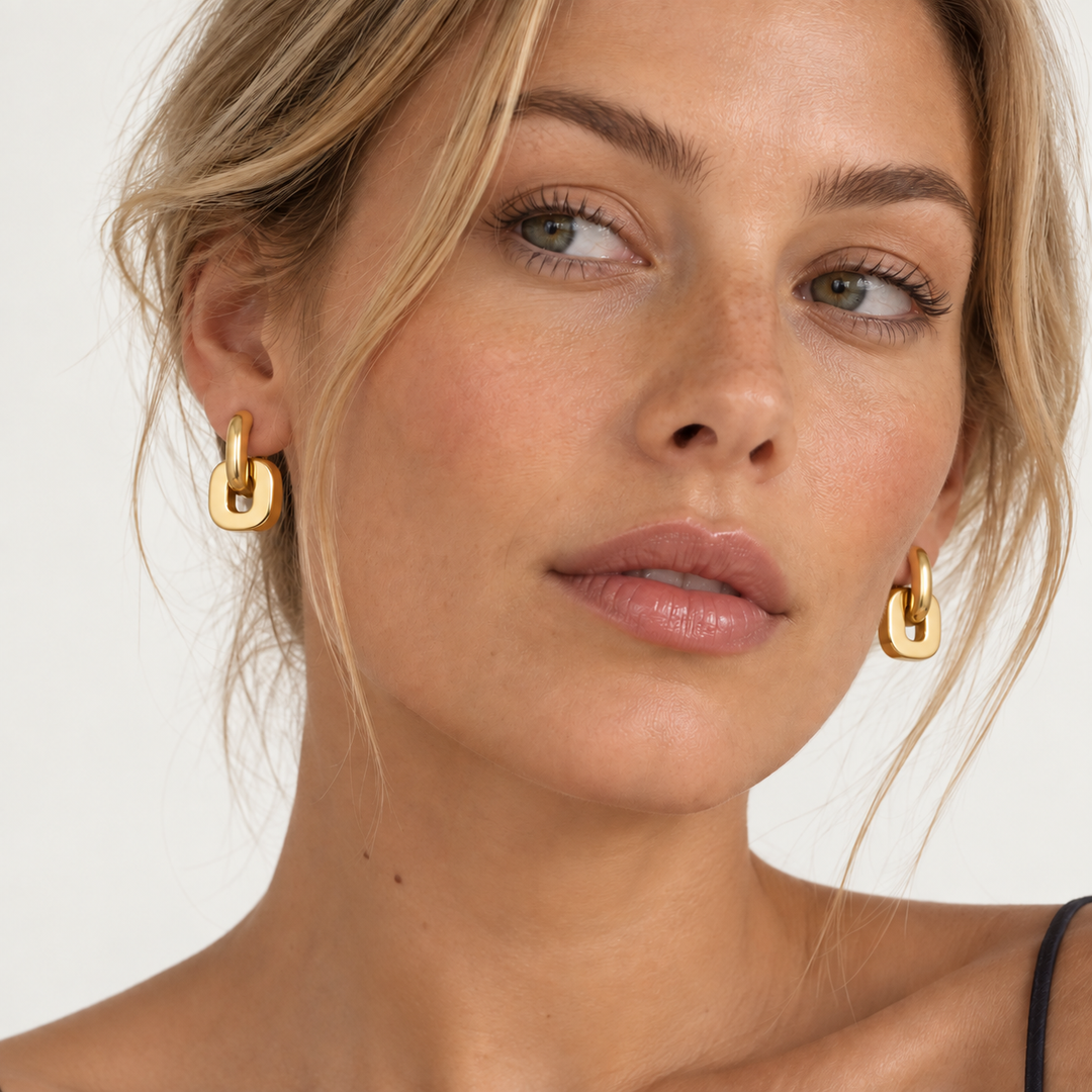 Close-up of a woman wearing gold hoop earrings with a thick, polished link design against a clean white background.