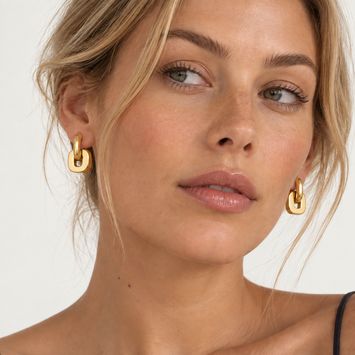 Close-up of a woman wearing gold hoop earrings with a thick, polished link design against a clean white background.