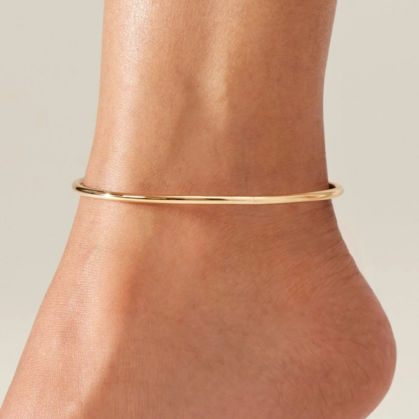 Gold anklet on a person's ankle against a neutral background
