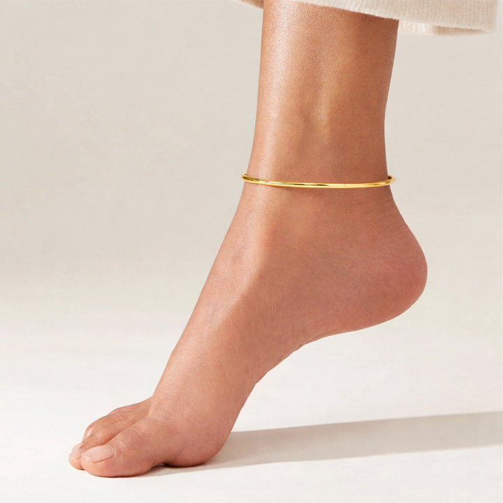 Gold anklet on a foot against a plain background