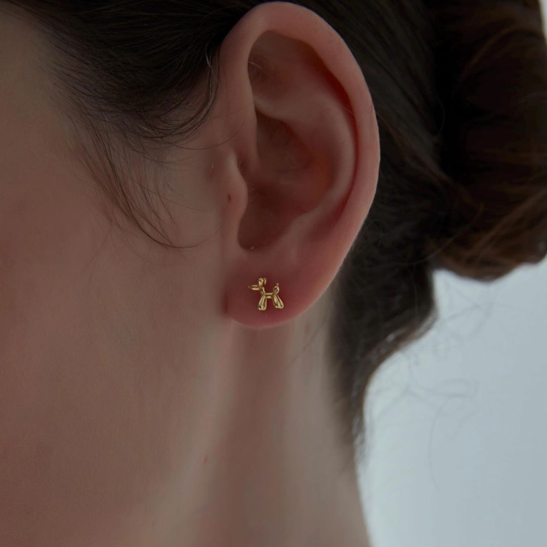 Gold dog-shaped earring on a person's ear with a neutral background