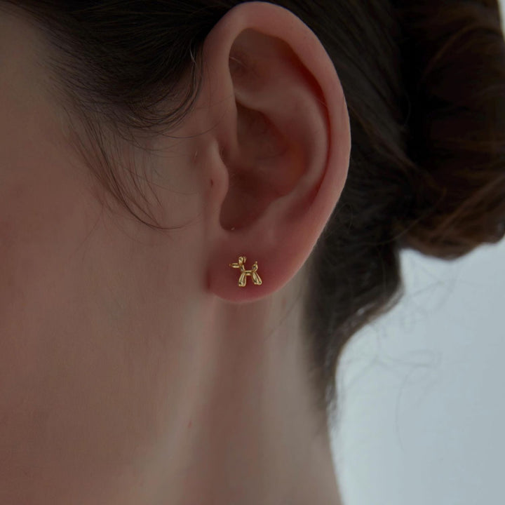 Gold dog-shaped earring on a person's ear with a neutral background
