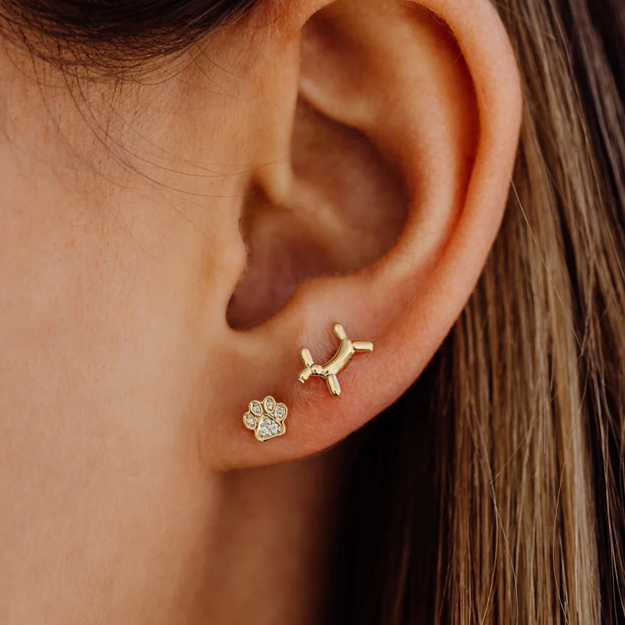 Close-up of an ear wearing gold dog-shaped and paw print earrings.