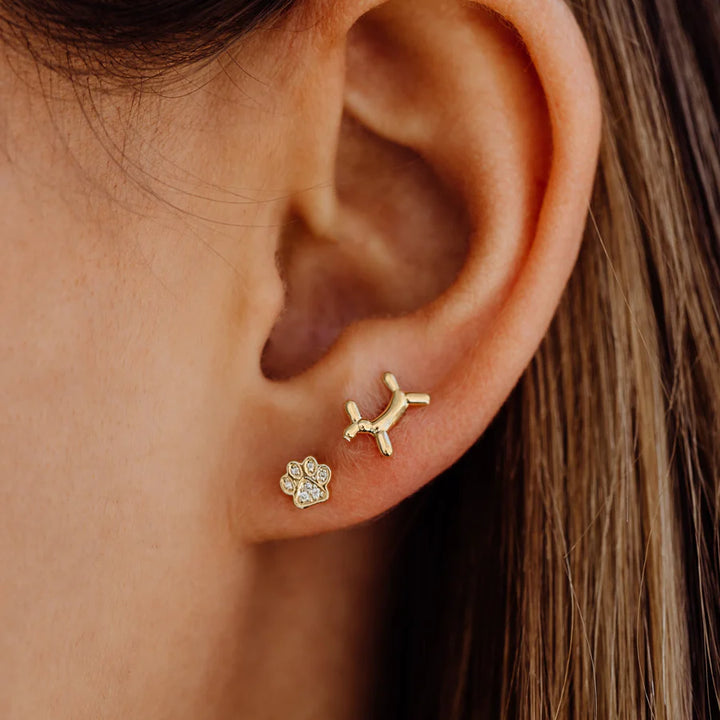 Close-up of an ear wearing gold dog-shaped and paw print earrings.
