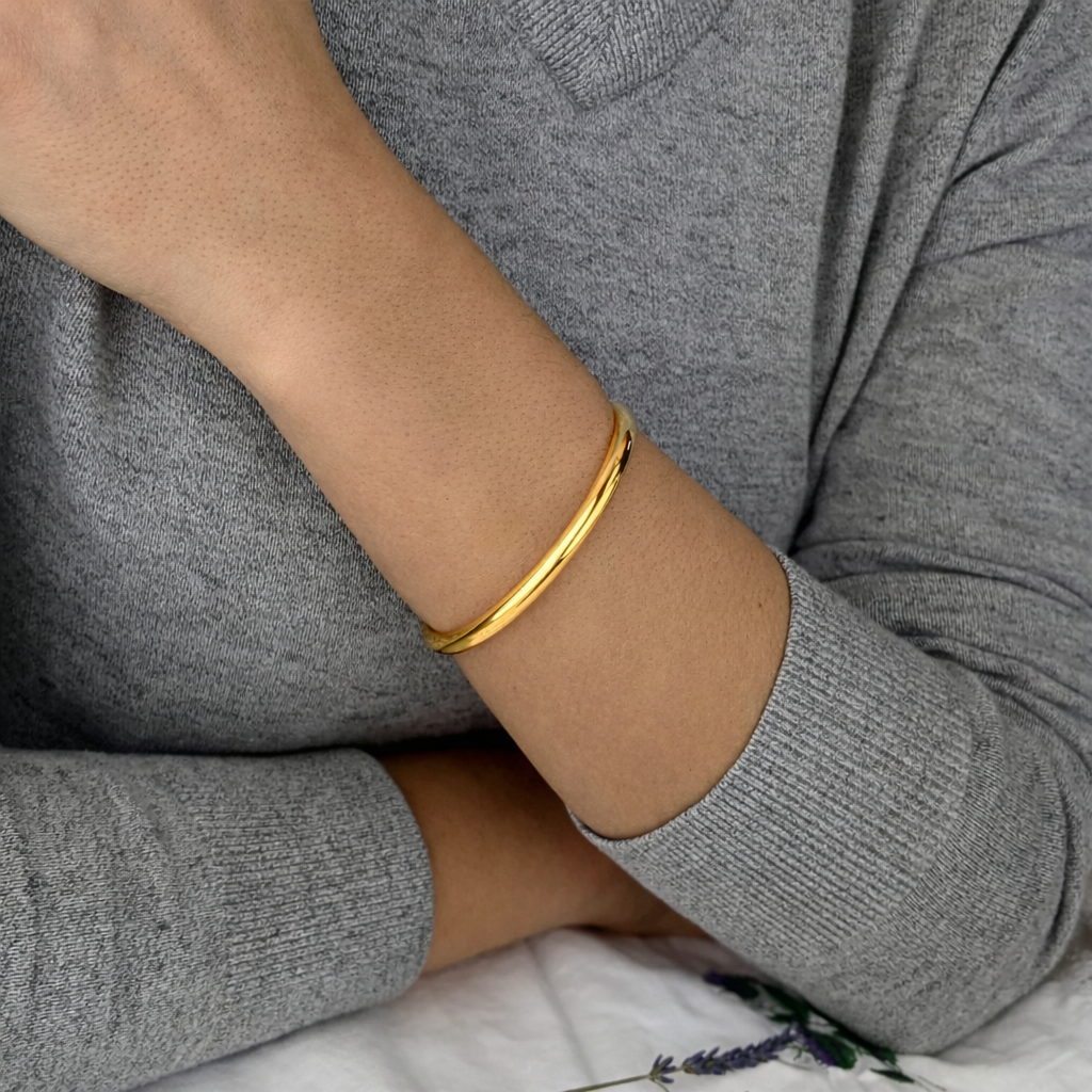Gold bracelet on a person's wrist with a gray sweater and floral fabric in the background