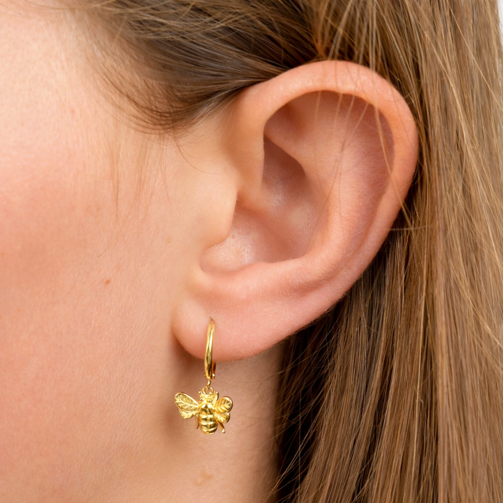 Gold bee-shaped earring worn by a person with brown hair.