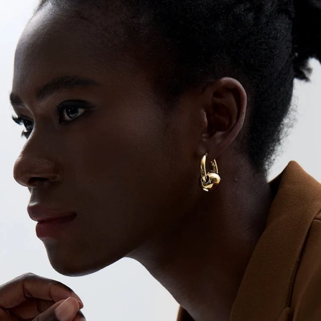 Close-up of a woman wearing gold hoop earrings with a neutral background