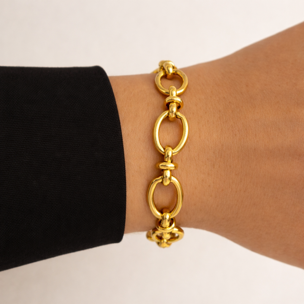 Gold chain bracelet on a wrist with a black sleeve against a beige background