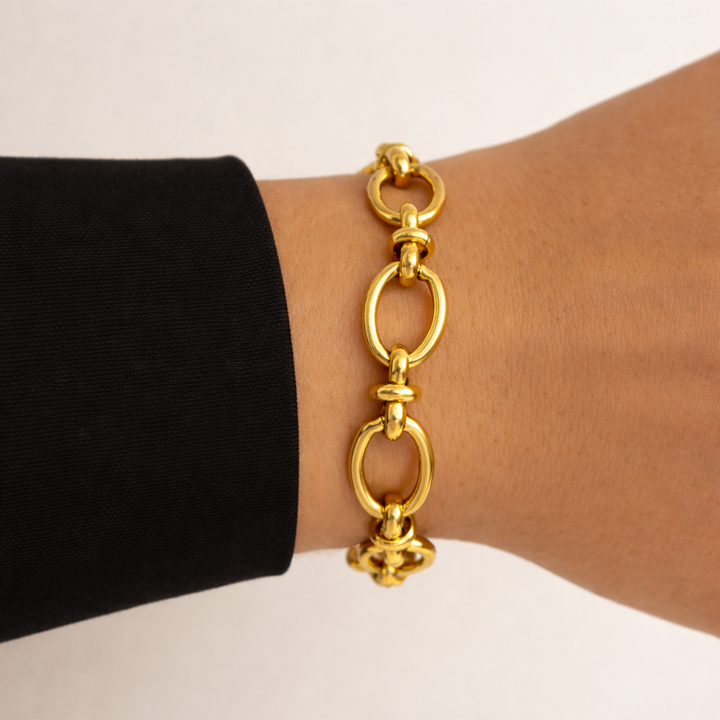 Gold chain bracelet on a wrist with a black sleeve against a beige background