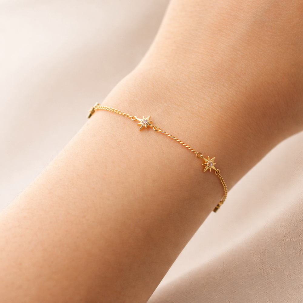 Gold bracelet with star charms on a wrist against a neutral background