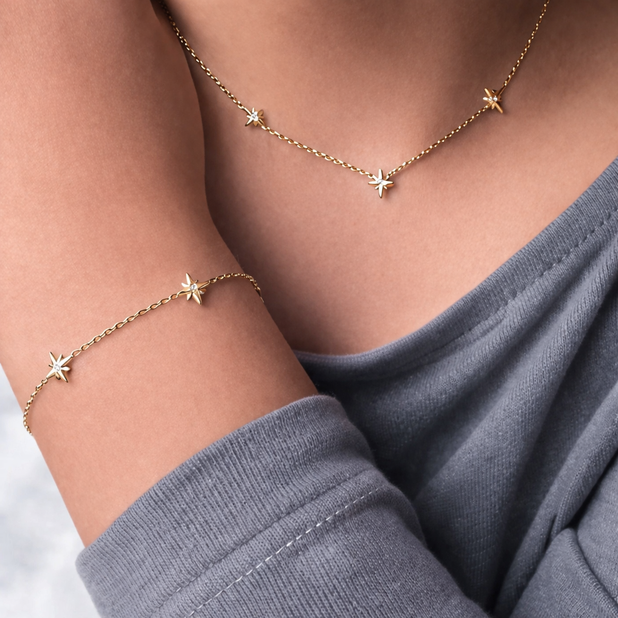 Gold star necklace and bracelet on a person wearing a gray top.
