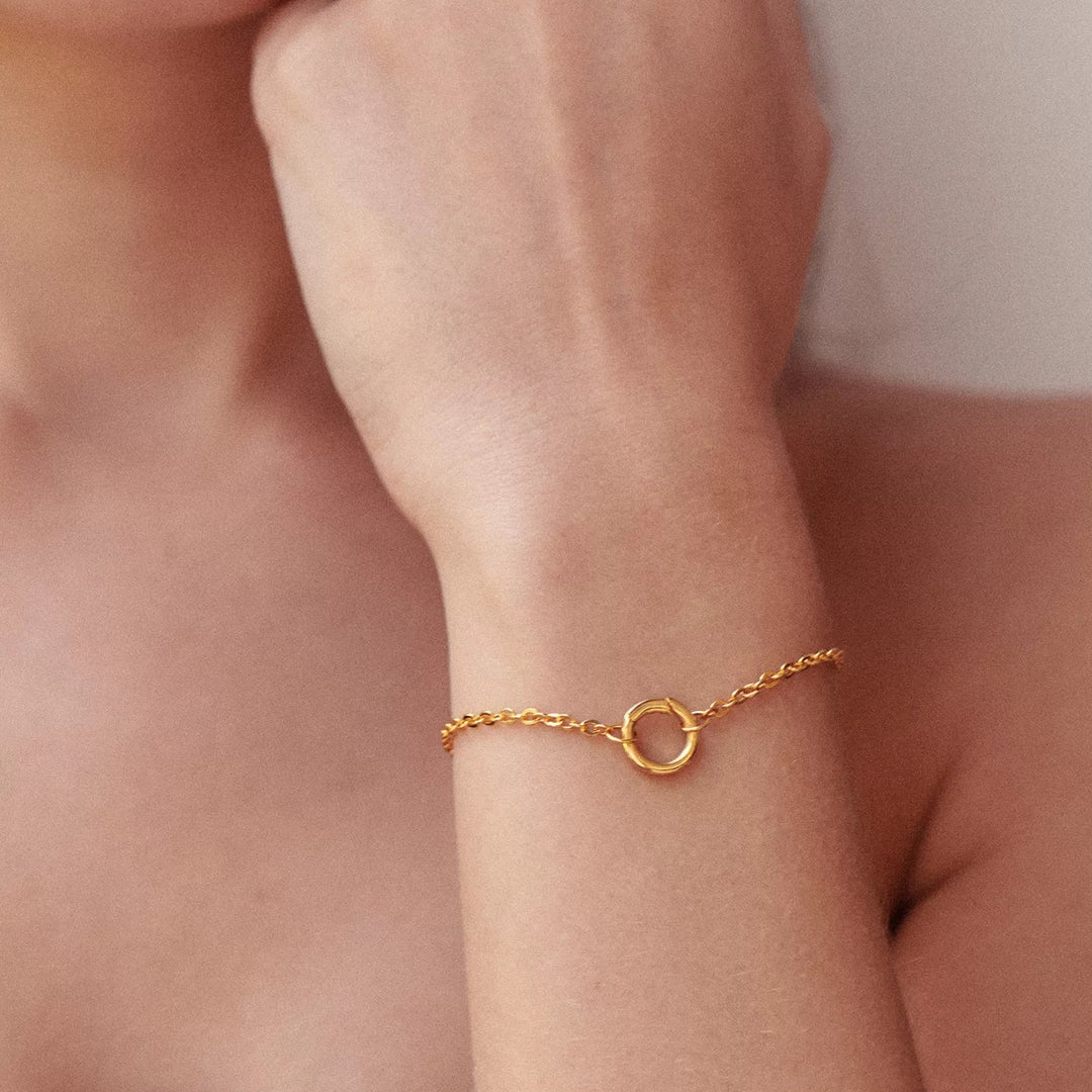 Close-up of a person wearing a gold bracelet on a neutral background