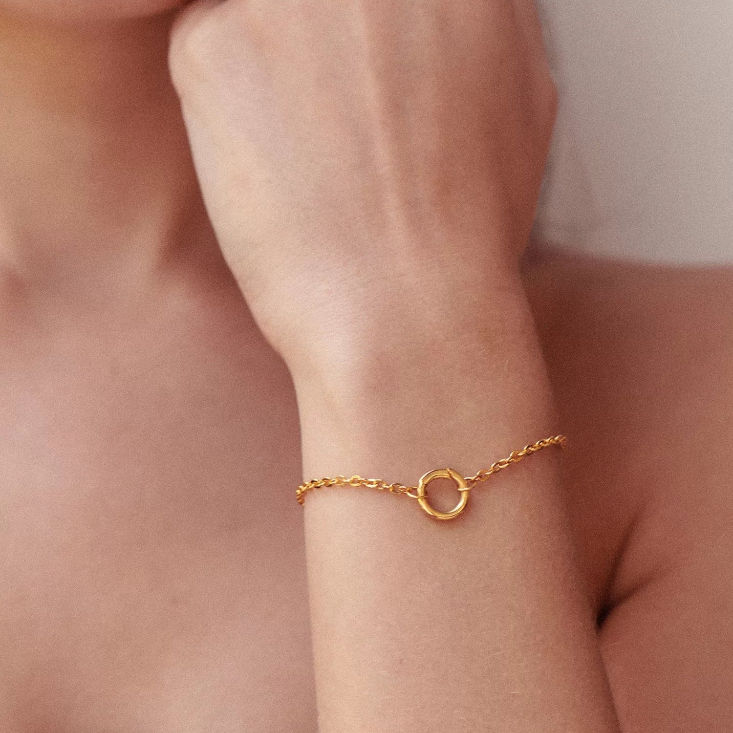 Close-up of a person wearing a gold bracelet on a neutral background