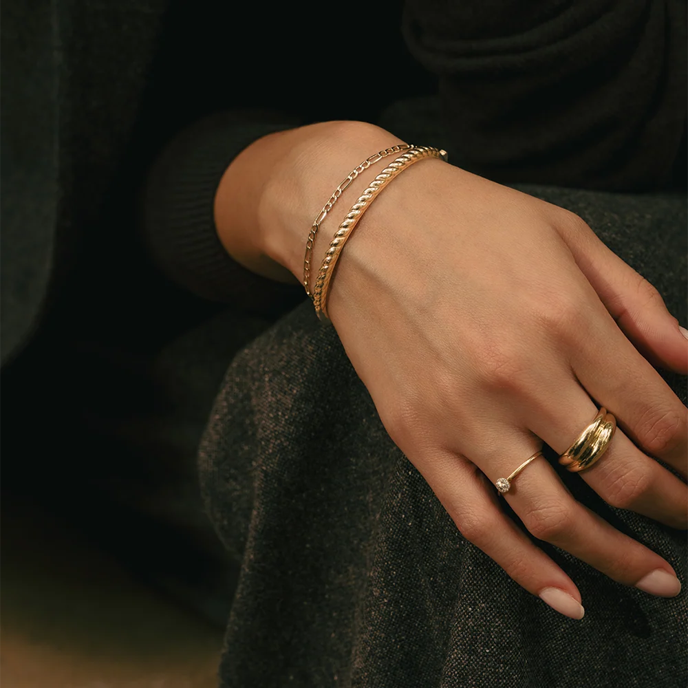 Hand wearing gold bracelets and rings on a dark background