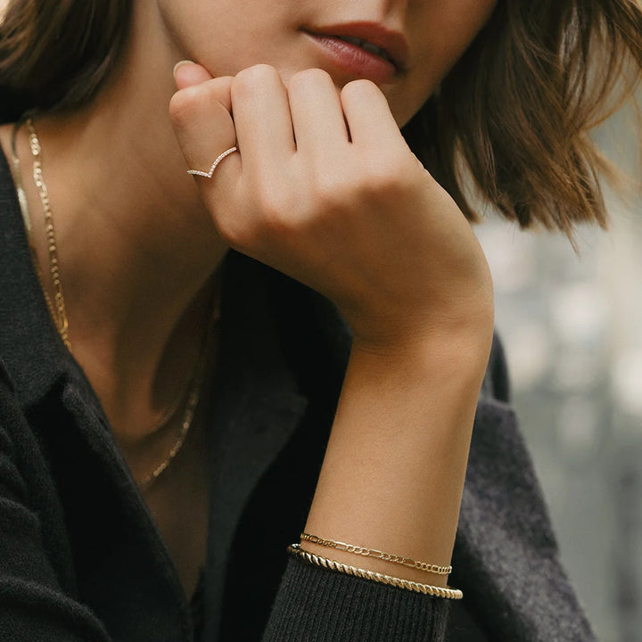 Close-up of a person wearing gold jewelry including a ring, necklace, and bracelet.