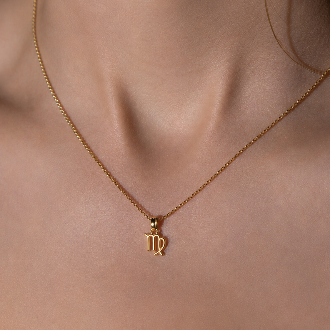 Gold necklace with a virgo pendant on a person's neck 