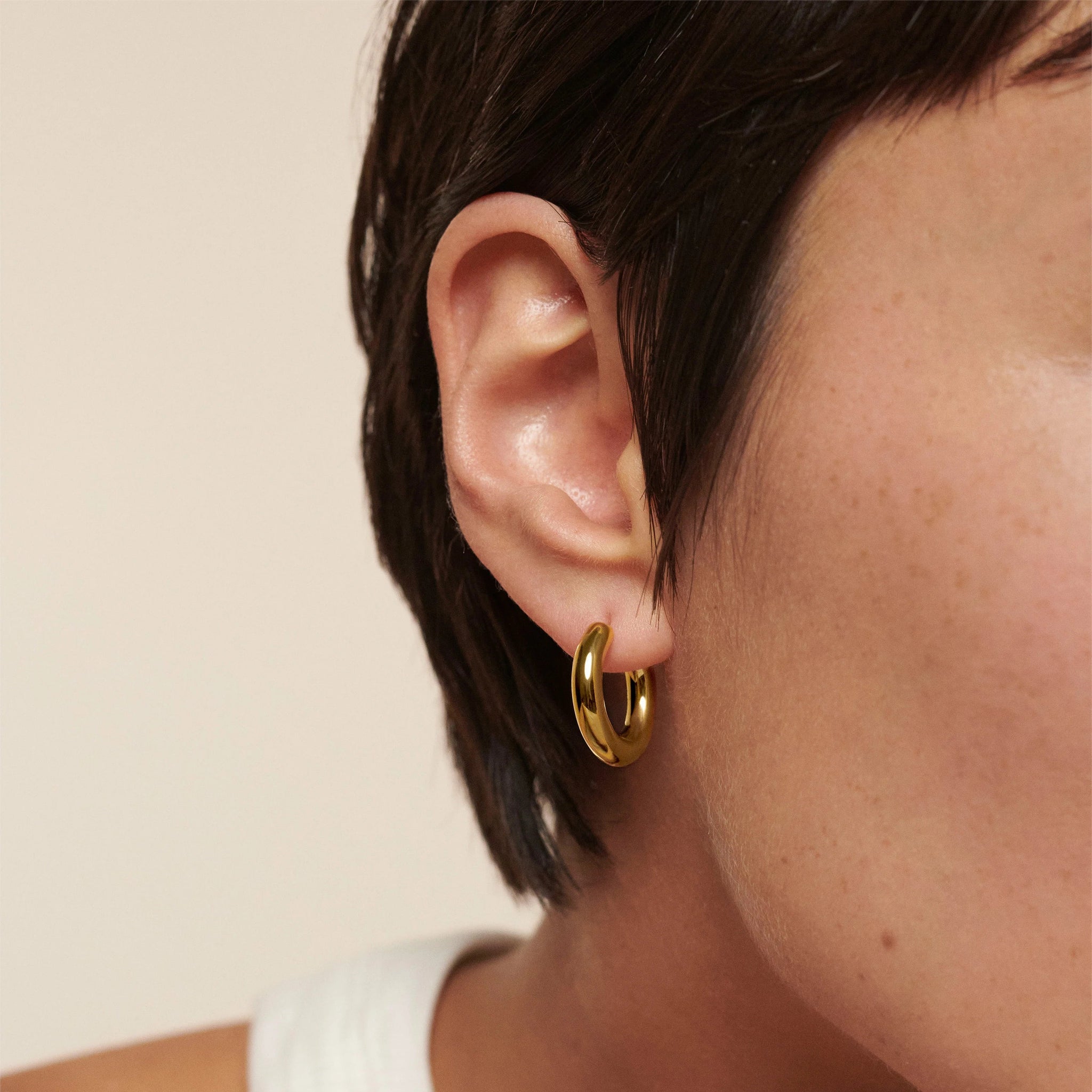 Close-up of an ear wearing a gold hoop earring with a neutral background