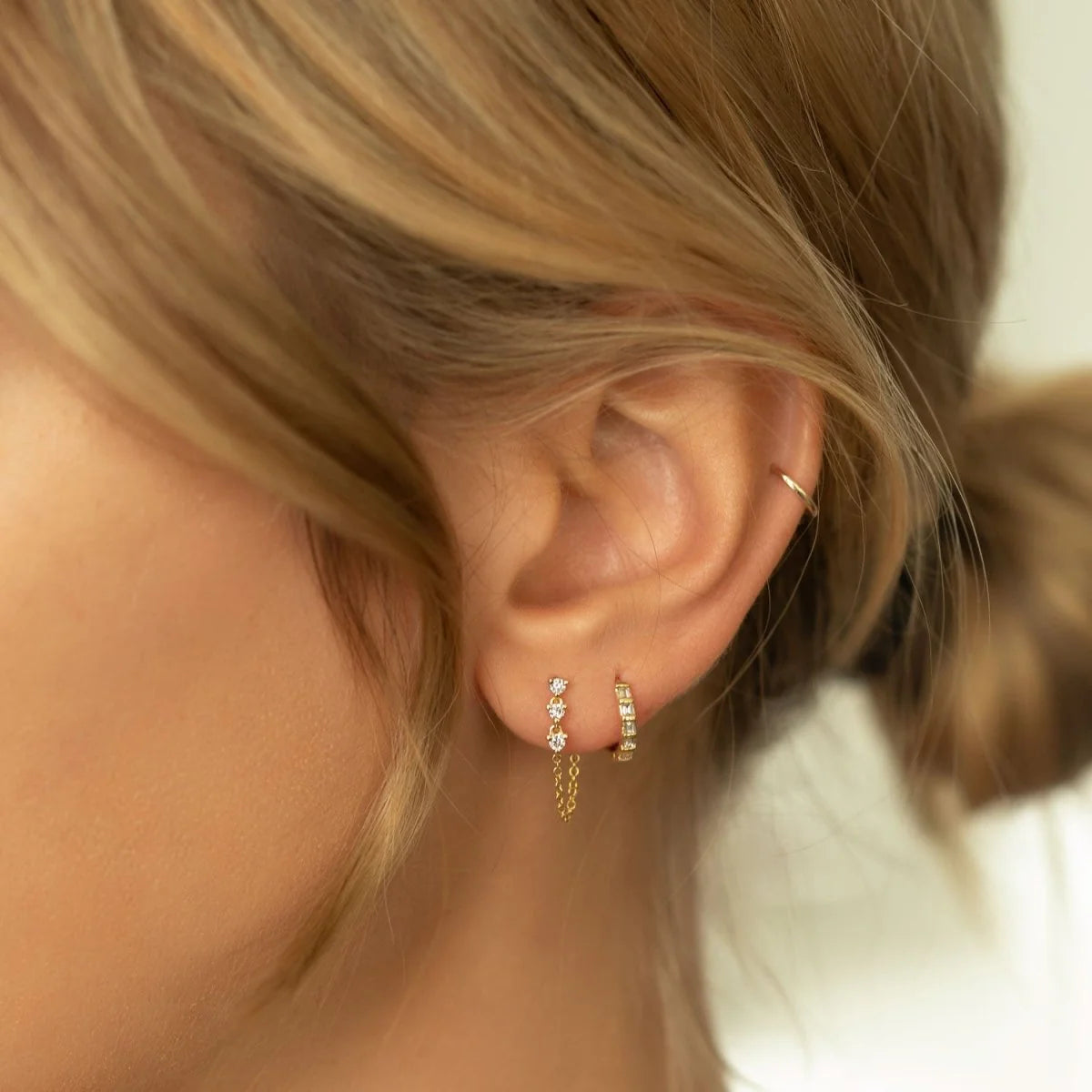 Close-up of an ear wearing gold hoop earrings with a blurred background