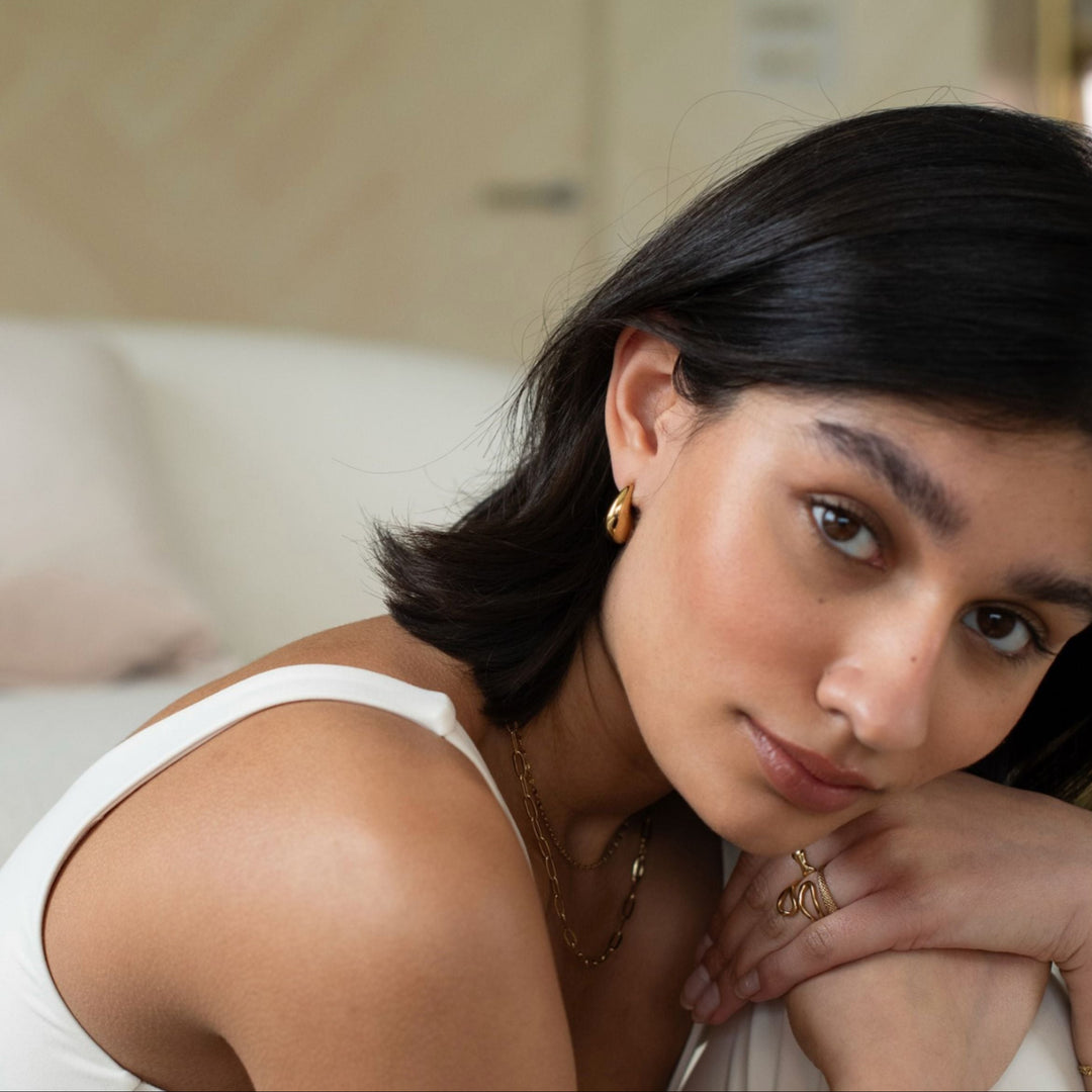Woman wearing gold earrings and a necklace in a neutral indoor setting