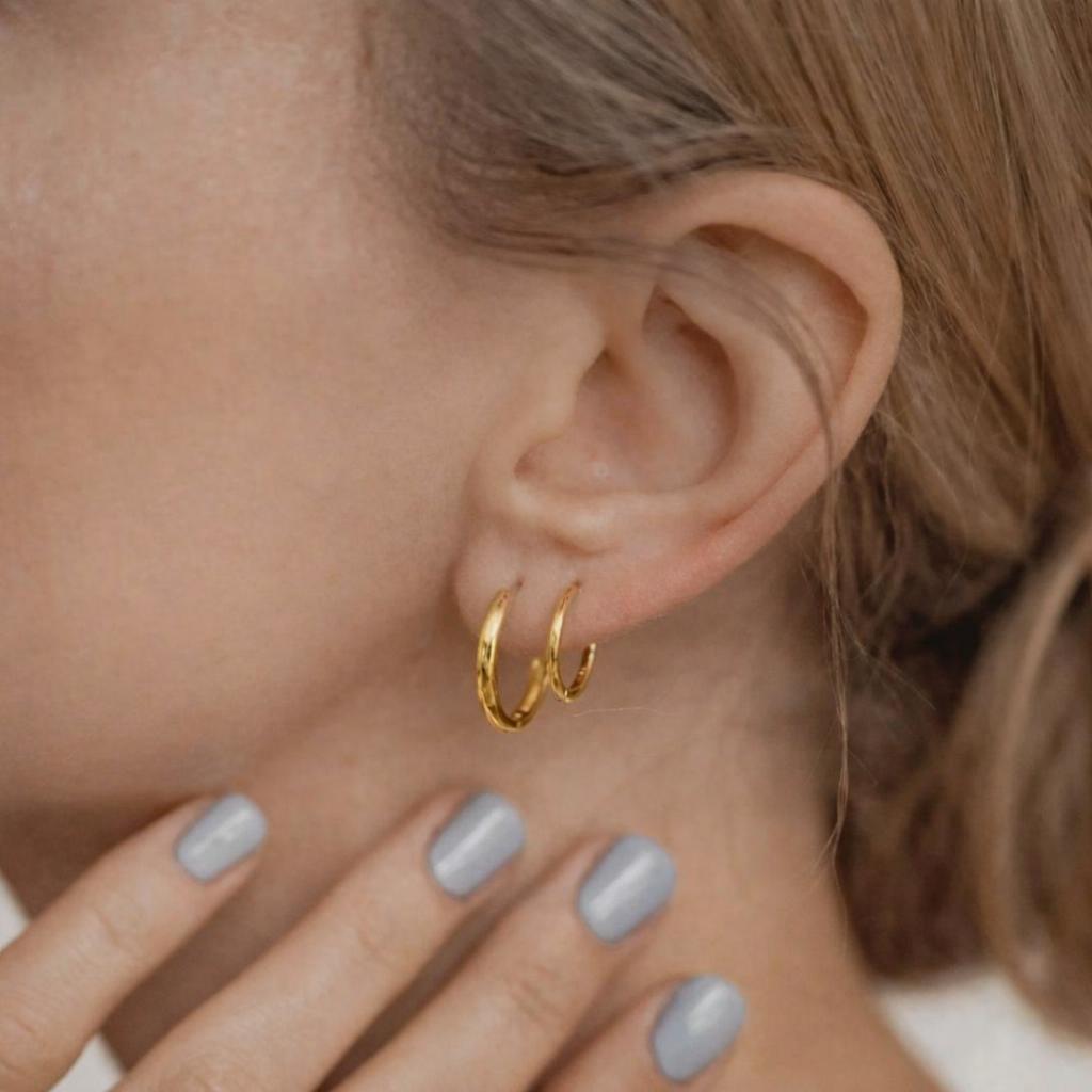 Close-up of a person wearing gold hoop earrings with a blurred background