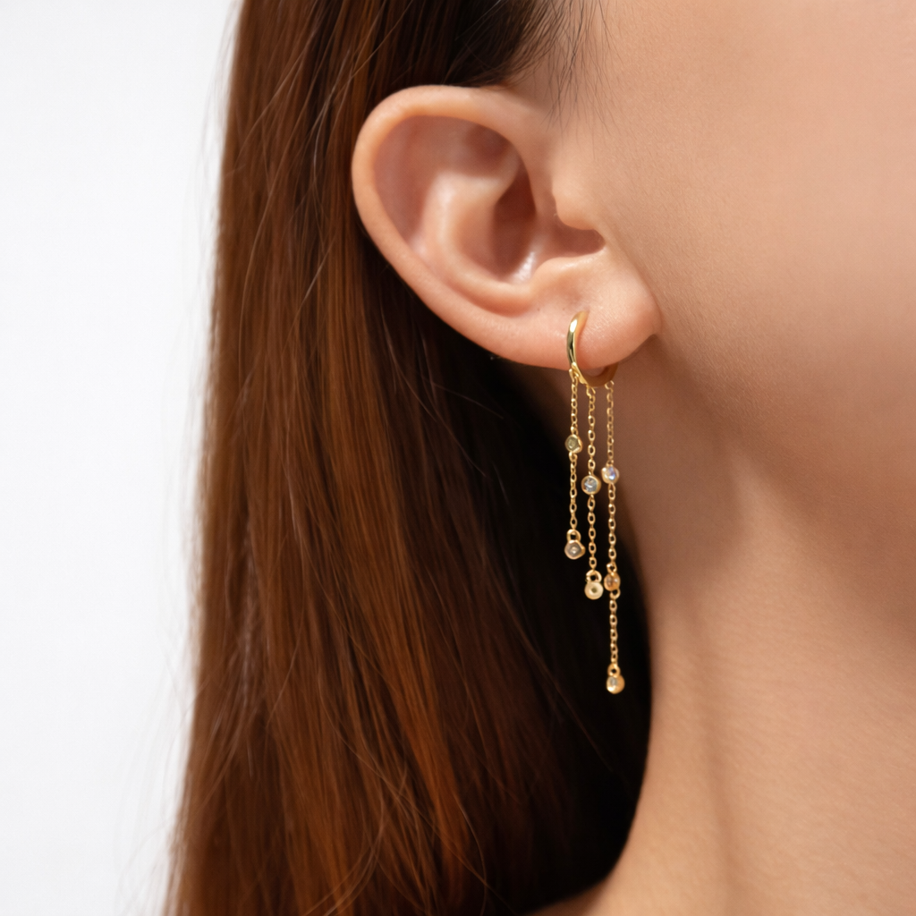 Gold earrings with dangling beads worn by a person with long brown hair.