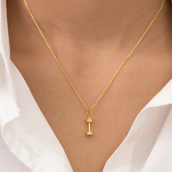 Gold necklace with a small pendant worn by a person in a white shirt.