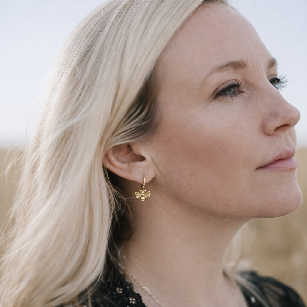 Close-up of a woman wearing gold bee earrings with a blurred background