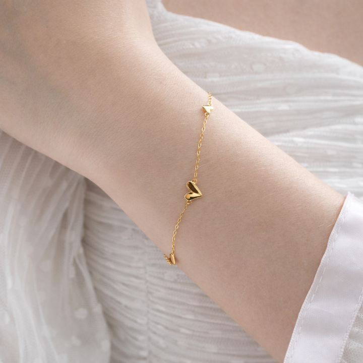 Gold bracelet with heart-shaped charms on a wrist against a neutral background
