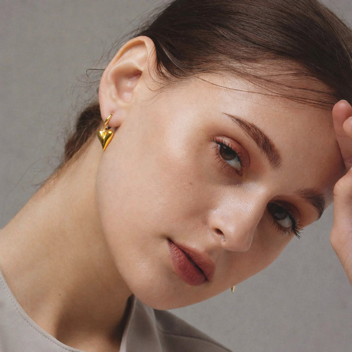 Close-up of a woman wearing gold heart-shaped earrings against a neutral background