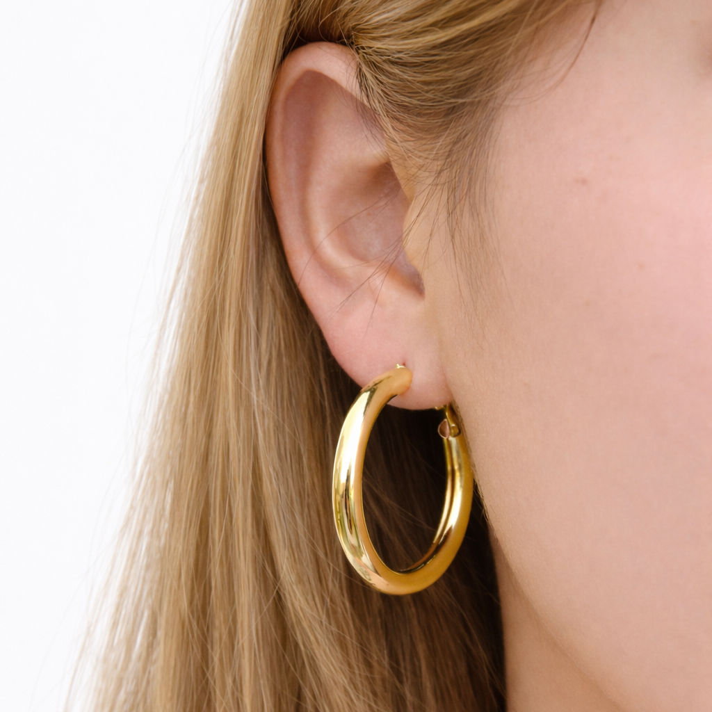 Gold hoop earring worn by a person with blonde hair on a white background