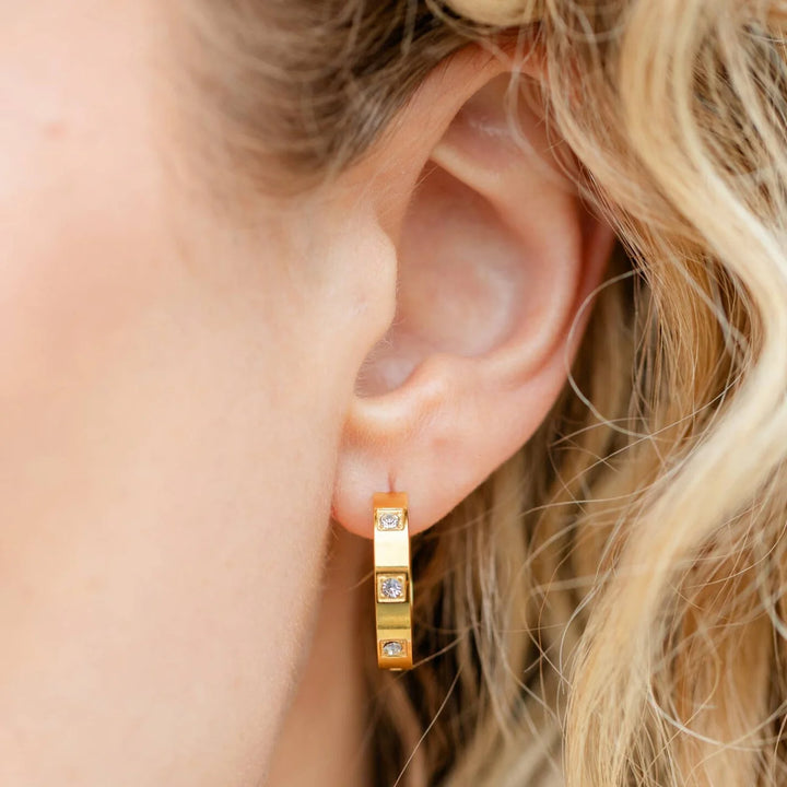 Gold hoop earrings with small diamonds worn by a person with blonde hair.