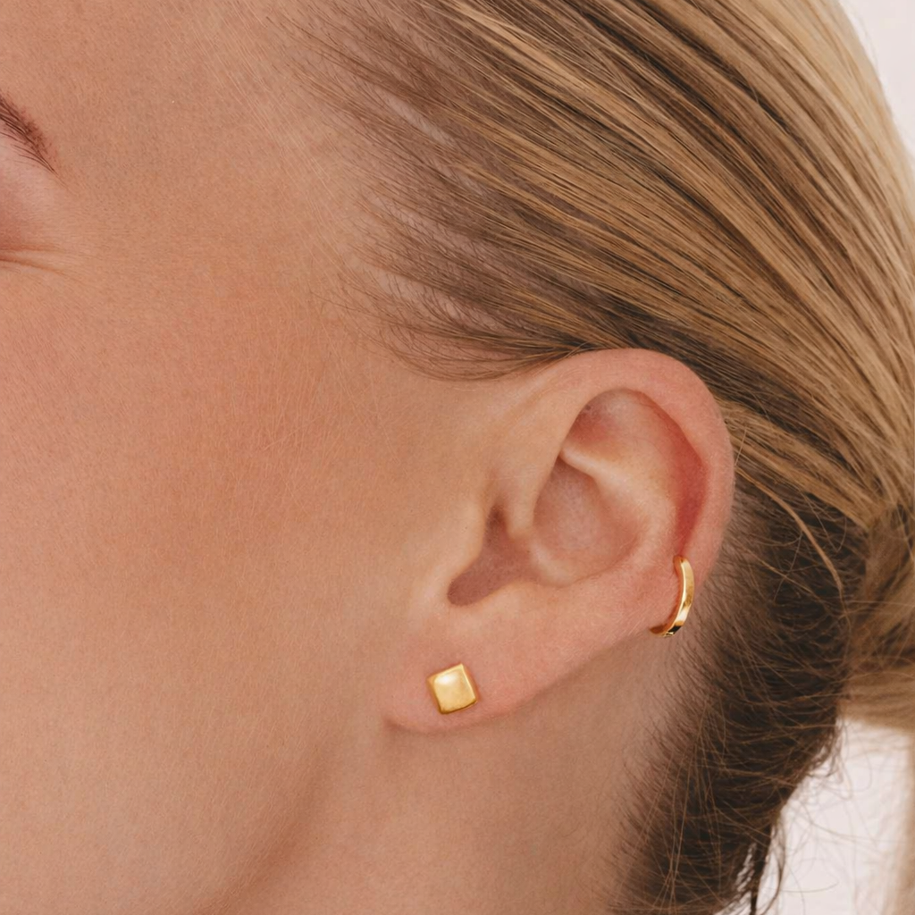 Close-up of a person wearing gold square stud earrings.