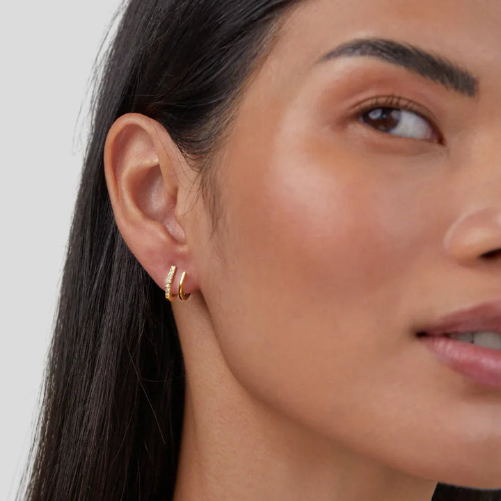 Close-up of a woman wearing a gold hoop earring against a neutral background