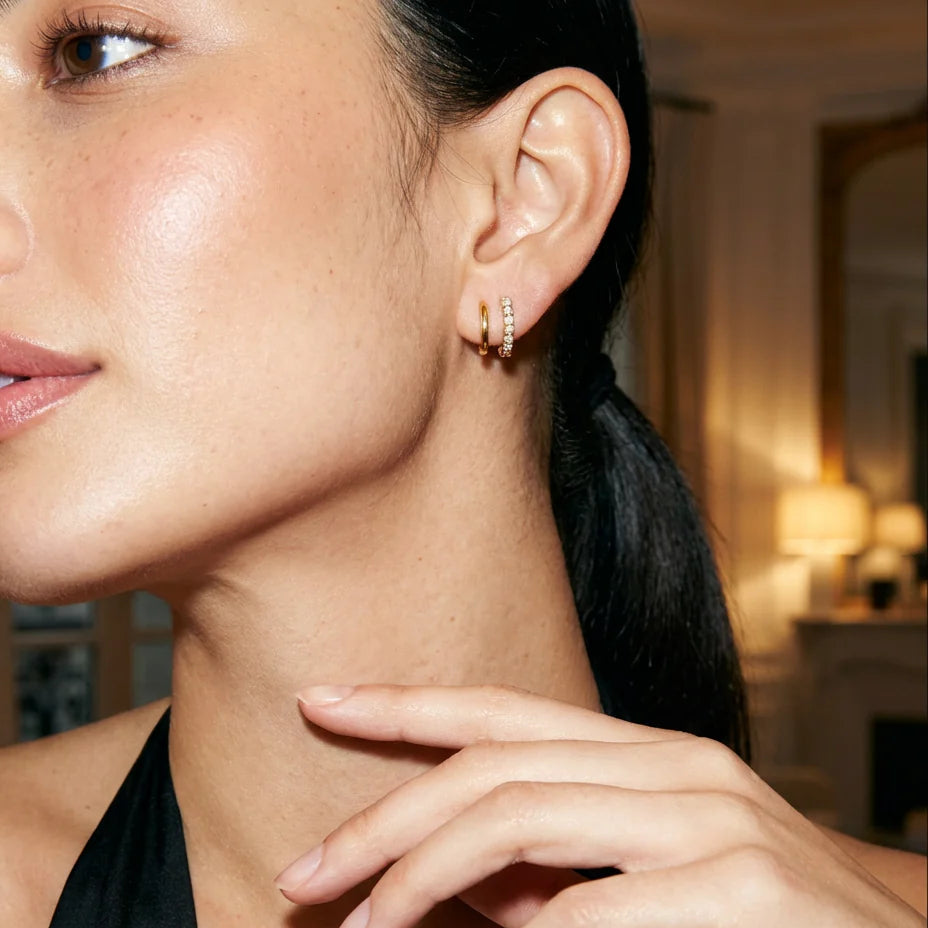 Close-up of a woman wearing gold hoop earrings with a blurred indoor background
