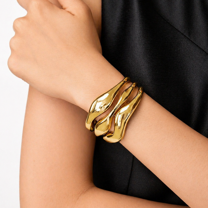 Gold bracelet on a person's wrist with a black dress in the background