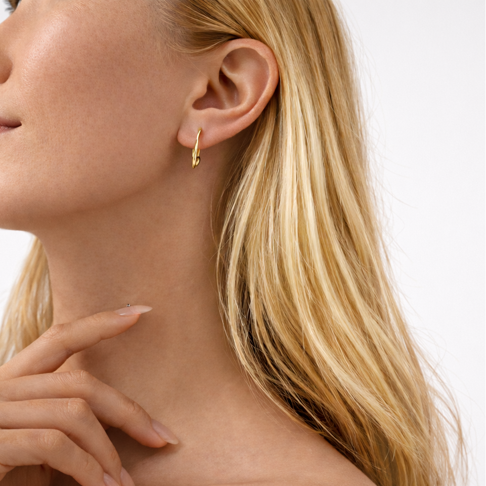 Close-up of a woman wearing gold hoop earrings with a plain background