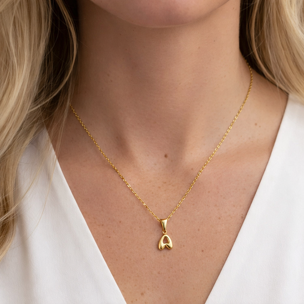 Gold necklace with a letter necklace pendant worn by a person against a neutral background