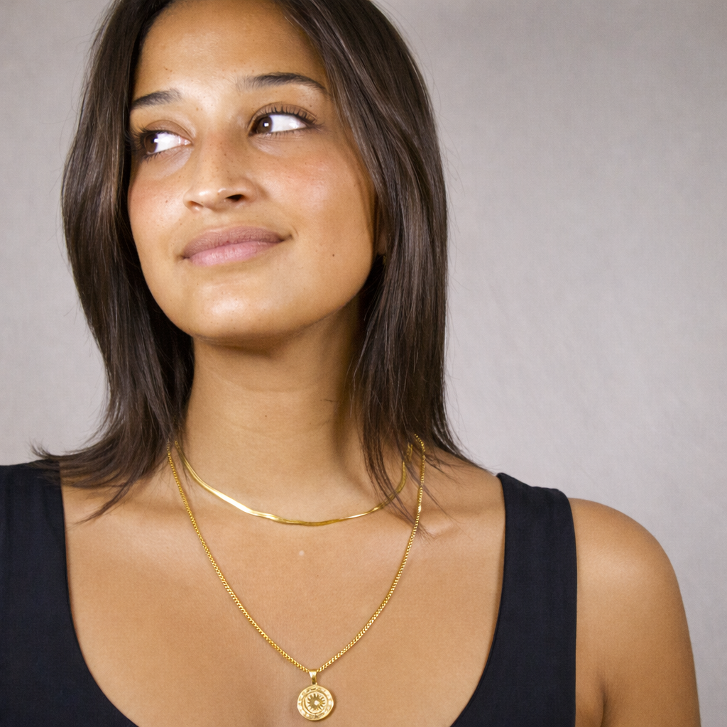 Woman wearing gold necklaces against a neutral background