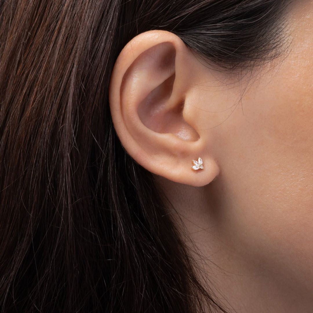 Close-up of an ear wearing a delicate earring with dark hair and skin background