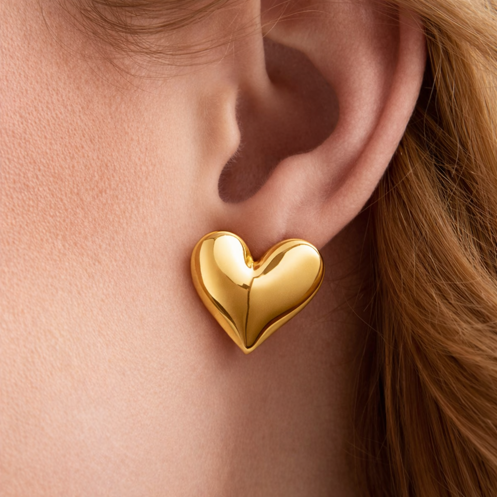 Gold heart-shaped earring worn on an ear with a blurred background