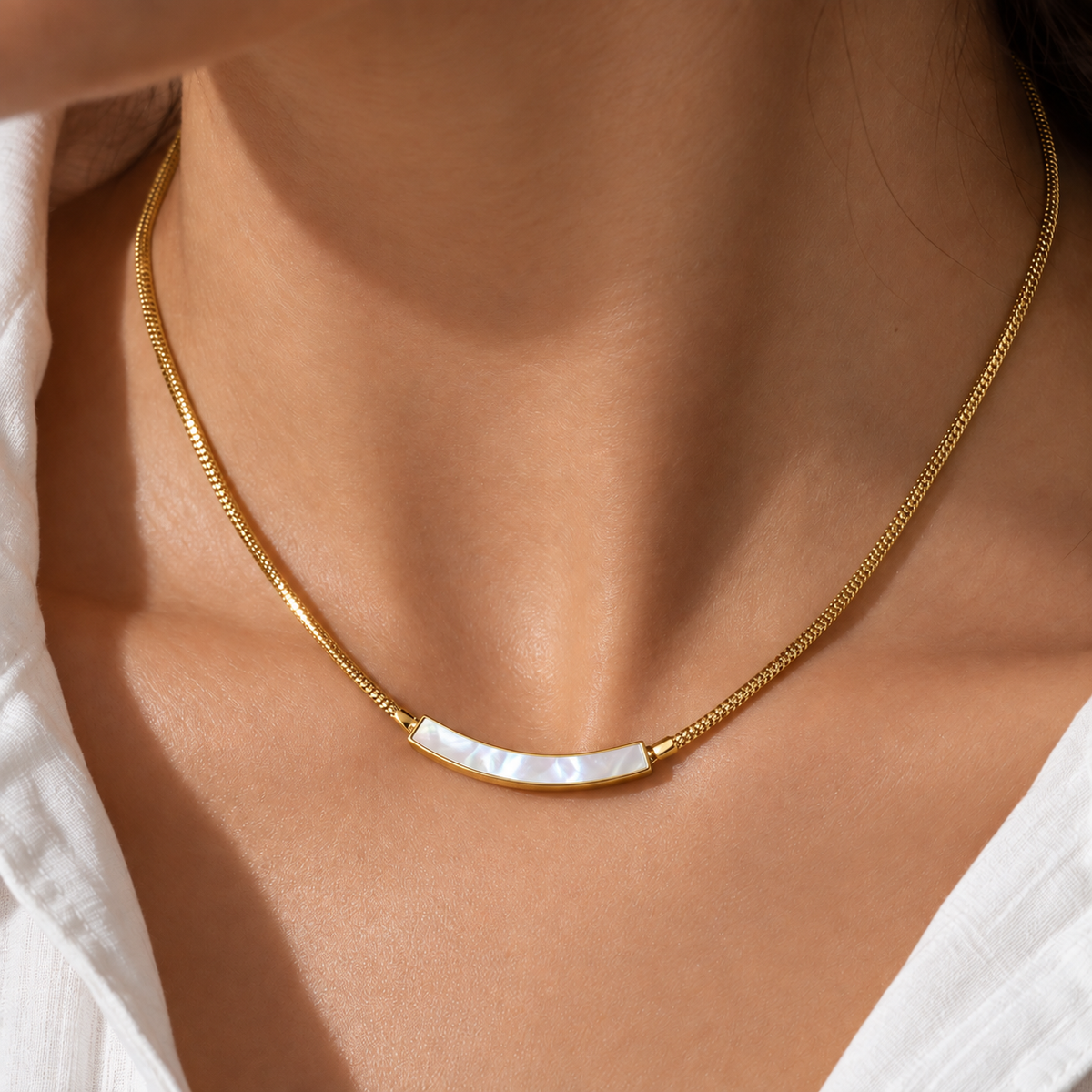 A close-up of a gold chain necklace with a curved white mother-of-pearl bar pendant, worn on a model's neck.
