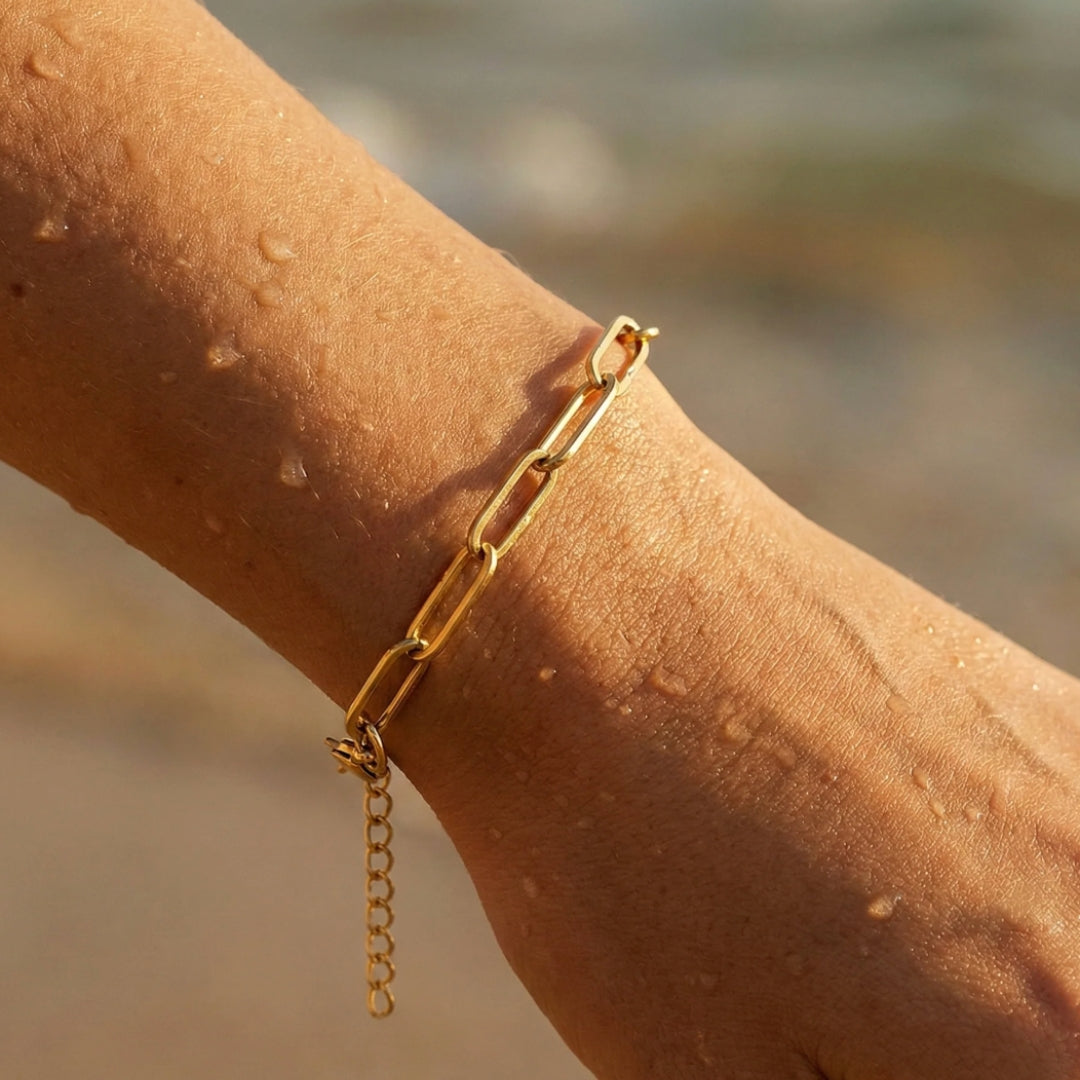 Gold chain bracelet on a wrist with a blurred beach background