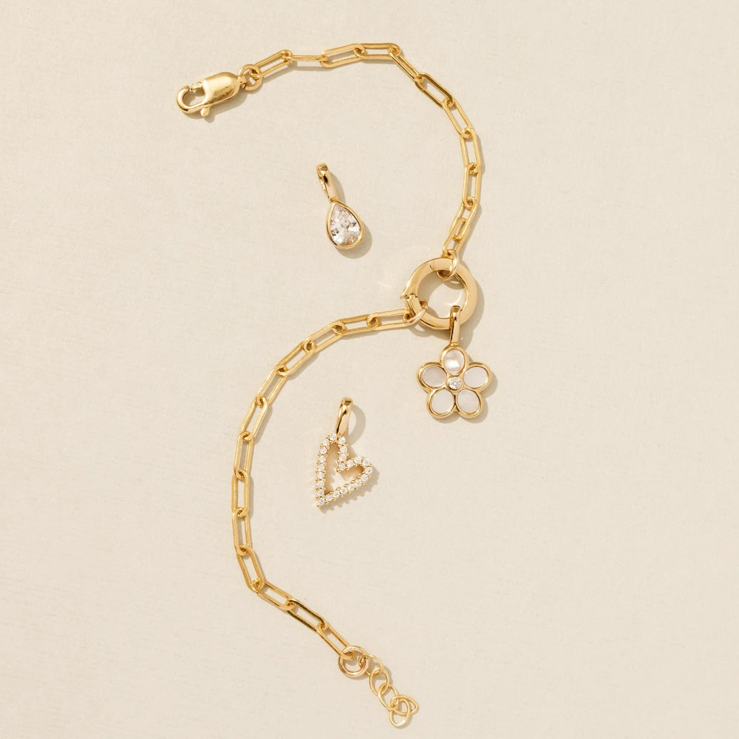 Gold chain bracelet with three charms on a beige background