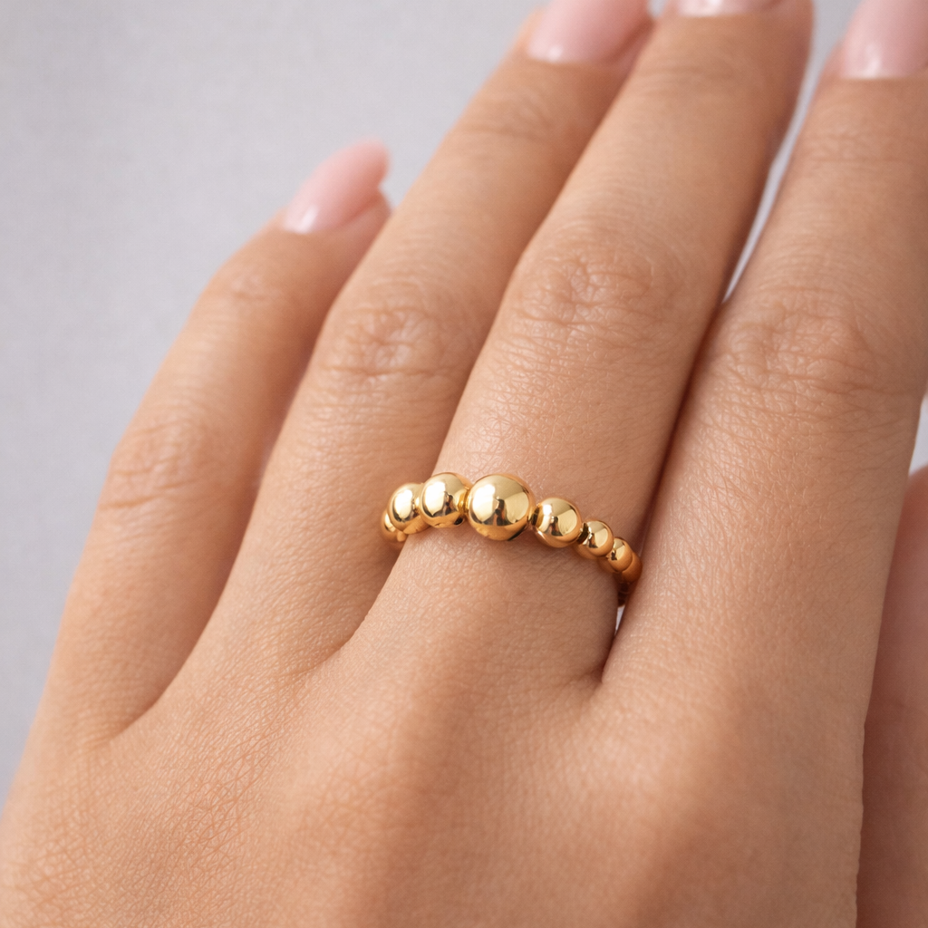 Gold beaded ring on a hand with a neutral background