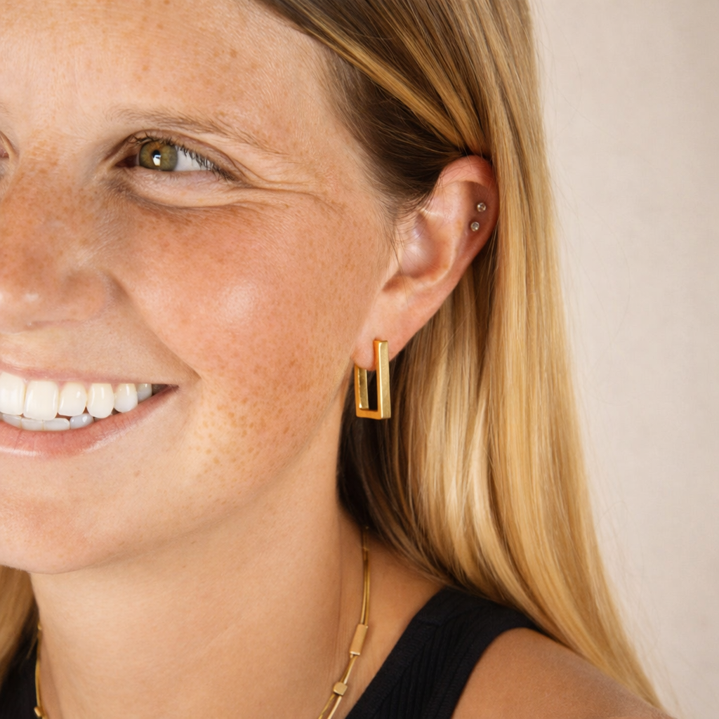 Close-up of a woman wearing gold hoop earrings with a neutral background