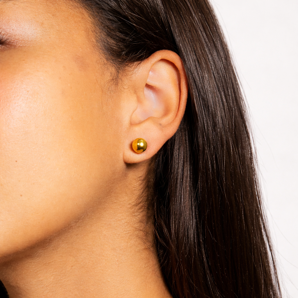Close-up of an ear wearing a gold earring with a plain background