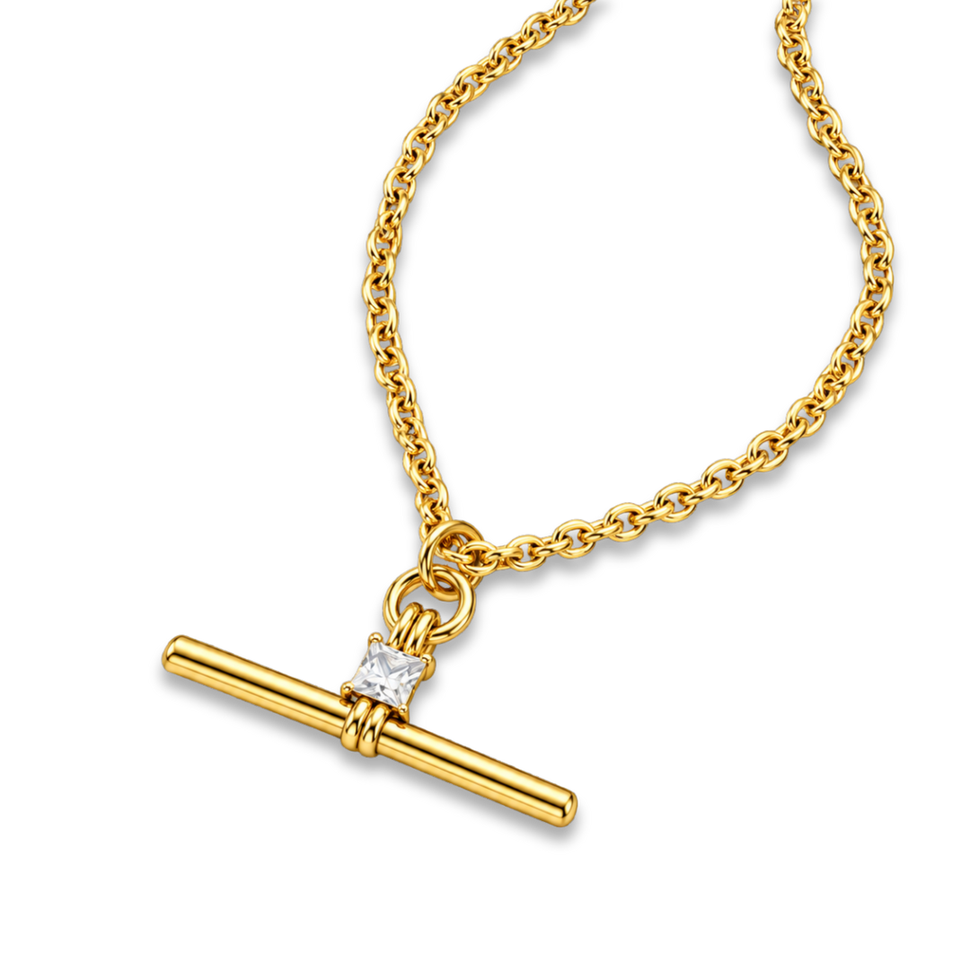 A gold chain necklace with a toggle bar pendant and a small clear gemstone accent, shown on a plain white background.