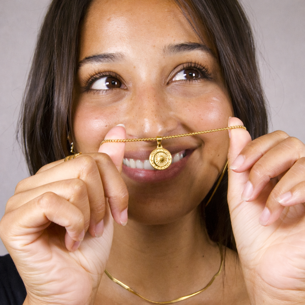 Woman holding a gold necklace with a pendant close to her face